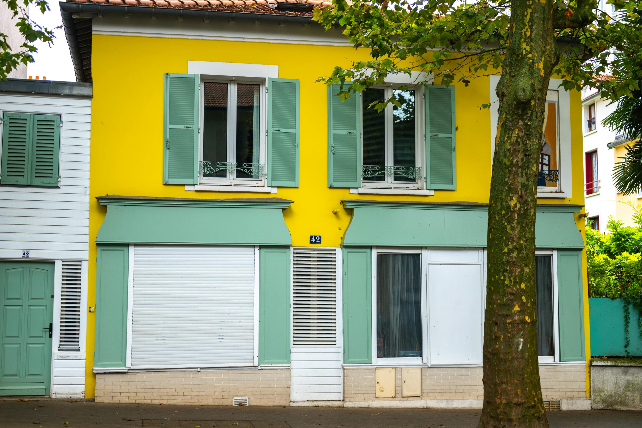 Colorful facade of a yellow house with green shutters in Paris, France.