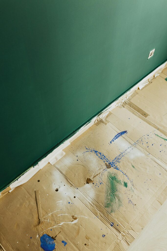 A newly painted green wall with cardboard protecting the floor during a home renovation.
